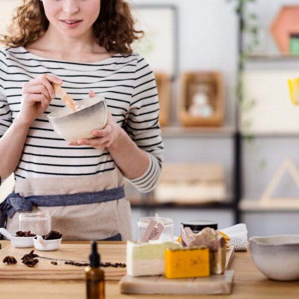Woman in an apron mixing ingredients in a bowl while making homemade skincare or beauty products. Natural DIY cosmetics with handmade soap, essential oils, and organic ingredients on a wooden table.