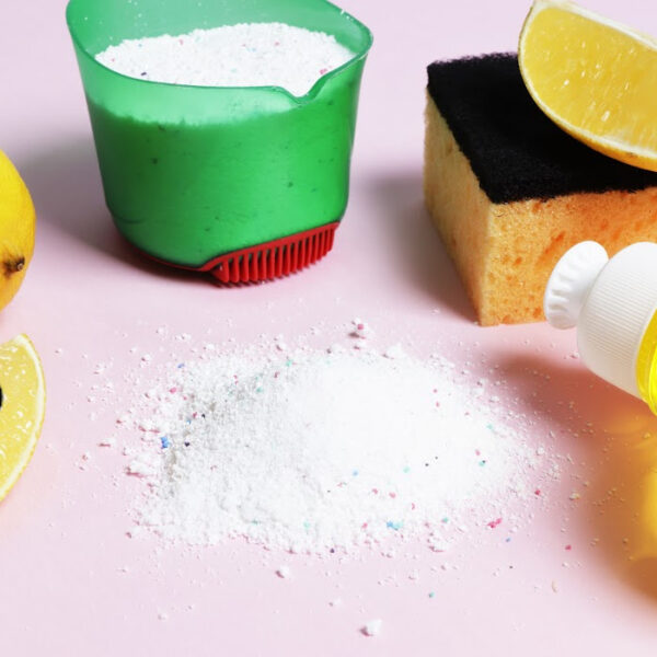Homemade cleaning supplies on a pink background, including natural ingredients like lemon, baking soda, and a sponge. DIY eco-friendly cleaning products for a non-toxic home.