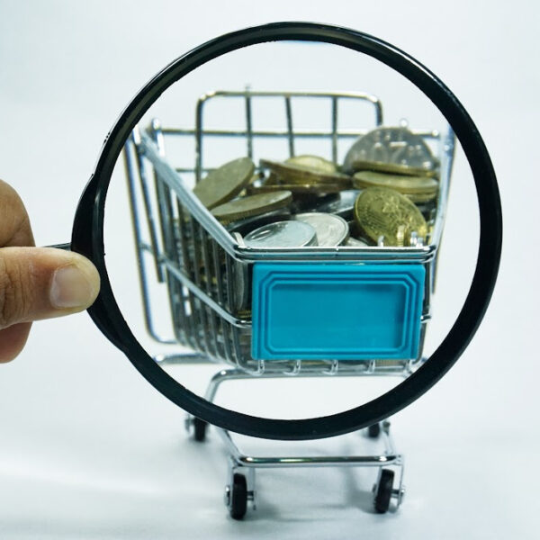 Mini shopping cart filled with coins, viewed through a magnifying glass. Concept of budgeting, saving money on groceries, and smart shopping strategies.