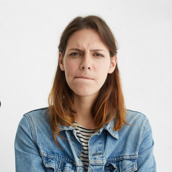 Woman with a skeptical expression in a denim jacket, biting her lip in thought—symbolizing self-doubt and hesitation linked to over planning and daily habits that feel productive but create mental roadblocks.